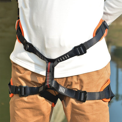 Person wearing a black and orange safety harness with a blurred natural background